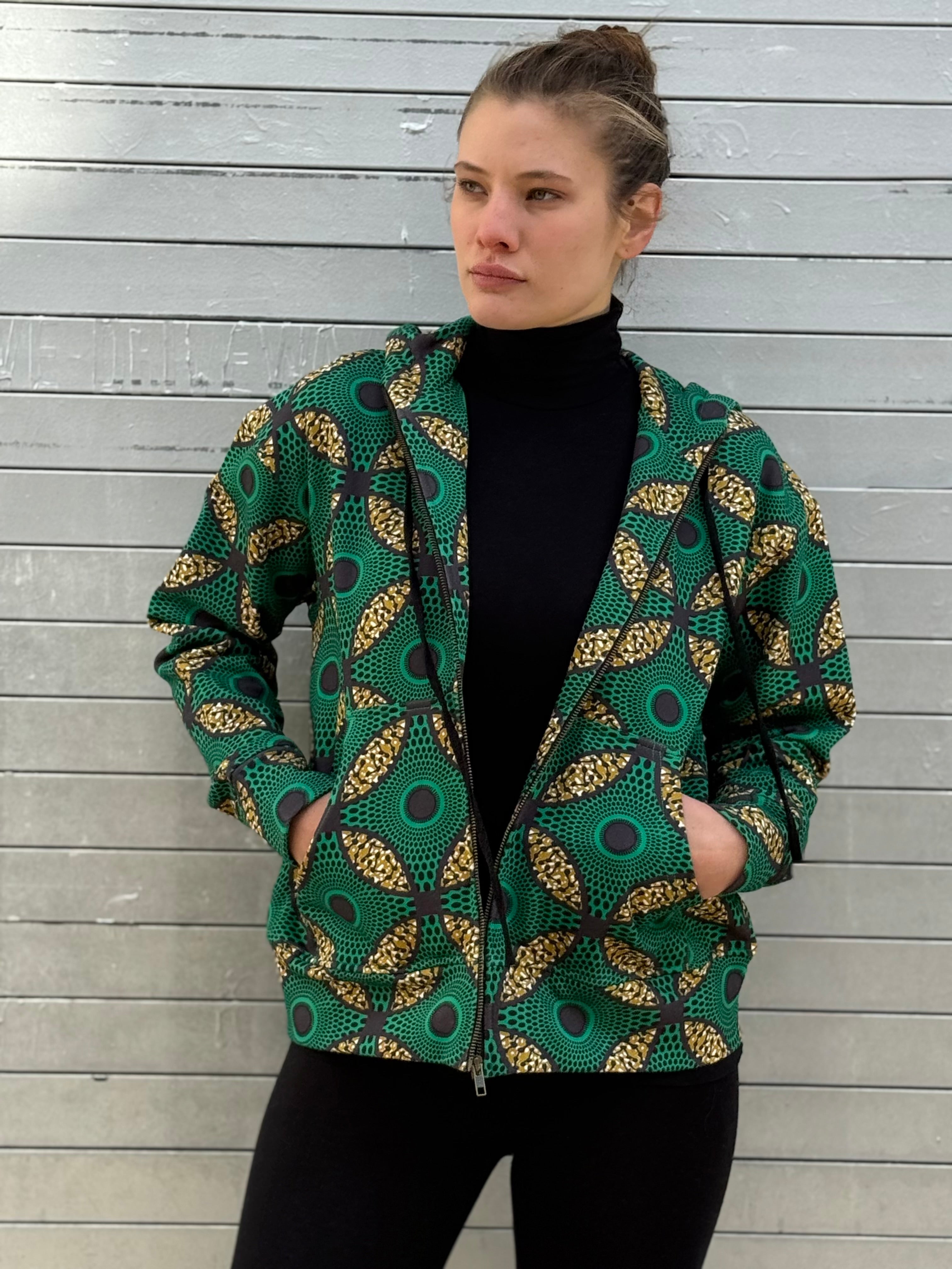 Model wearing the Ìmọ́lẹ̀ Green Zip-Up Hoodie by Lola Faturoti Loves, crafted from organic cotton and printed with eco-friendly inks. The Yoruba-inspired pattern in emerald green and gold brings light and warmth to winter days, embodying sustainable style and cultural elegance.